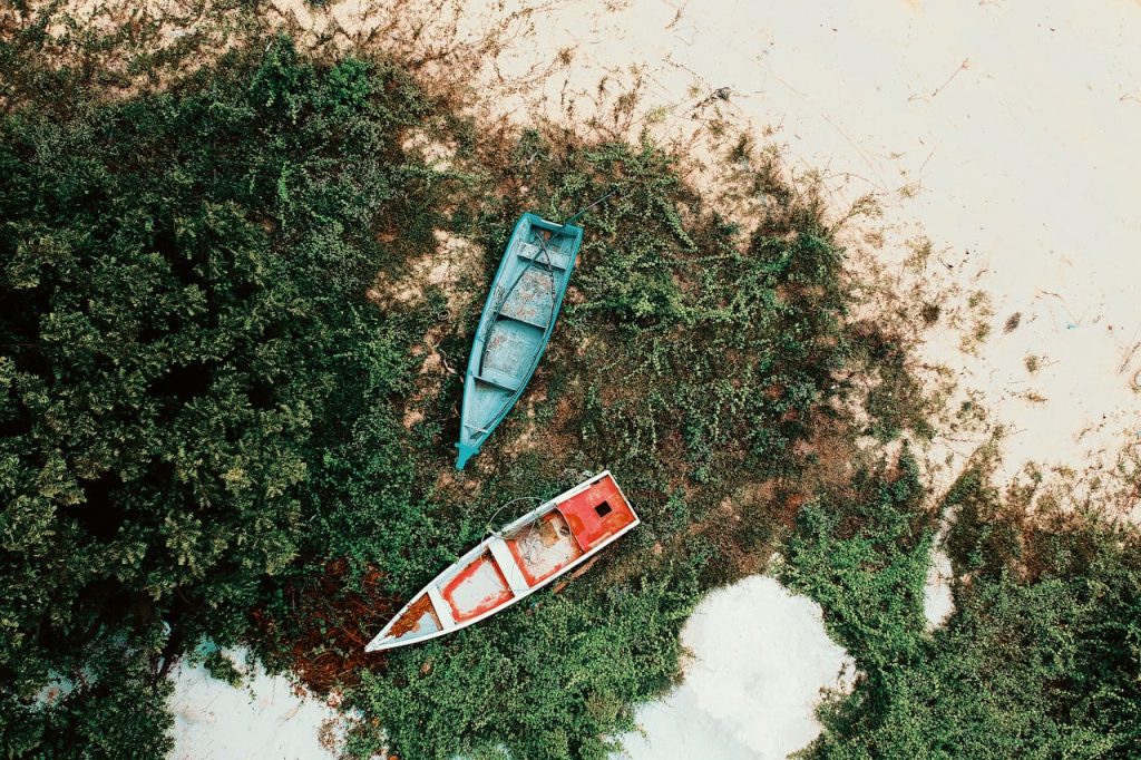 Aerial shot of two abandoned boats on a sandy shoreline in Balok, Malaysia, surrounded by greenery.